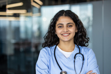 Smiling indian nurse wearing scrubs holding stethoscope