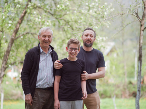 Three generations together: grandfather, father and smiling grandson in a spring garden family portrait