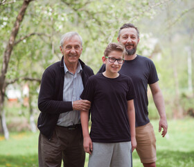 Obraz premium Three generations family portrait of grandfather, father and smiling grandson in a green garden