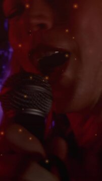 Vertical video: Female singer gripping mic singing music show causing camera close lights gold dust