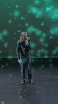 Vertical video: Singer starting as music playing holding mic moving right teal lights circling him