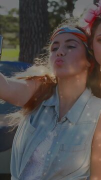Vertical video: Woman reaching phone selfie park posing tapping sharing social with sparkle overlay