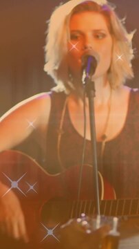 Vertical video: Cup raising zooming female singer strumming and singing for fans sparkling over her