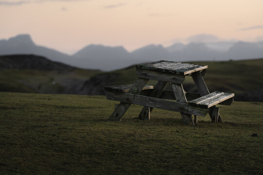 View of a weathered picnic table sits on a grassy bluff overlooking distant, misty mountains under a pale sky, Clachtoll Beach, Sutherland, Scotland.