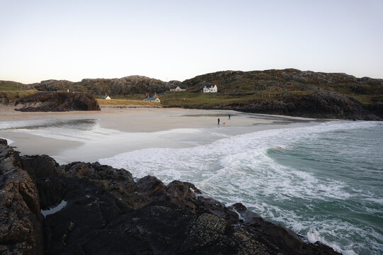View of the tranquil beach where the foamy waves meet the dark, rocky outcrops, framed by the rugged hills, Clachtoll Beach, Sutherland, Scotland.