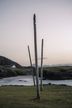 View of rustic wooden poles stand sentinel on a grassy bluff overlooking a serene, sandy cove as the sky fades into twilight, Clachtoll Beach, Sutherland, Scotland.