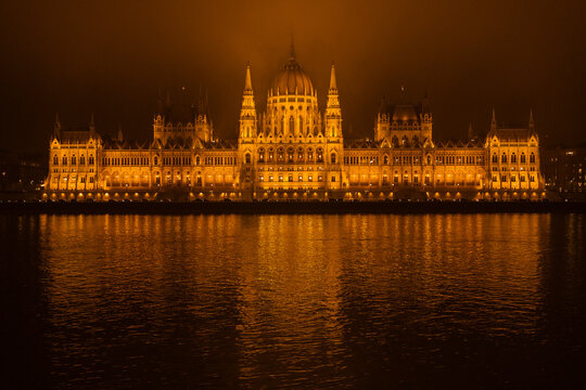 View of the Hungarian Parliament Building glows with warm, inviting lights, casting a mirrored reflection on the tranquil Danube River at night, Budapest, Hungary.