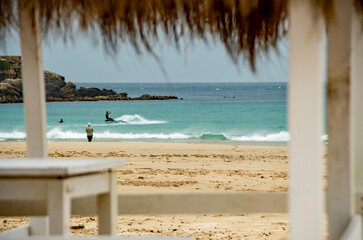 Kite surfers in the waves on a windy day. Spectators watch on the sandy beach, Bright colourful kites fill the cloudy sky. Turquoise water. copy space.