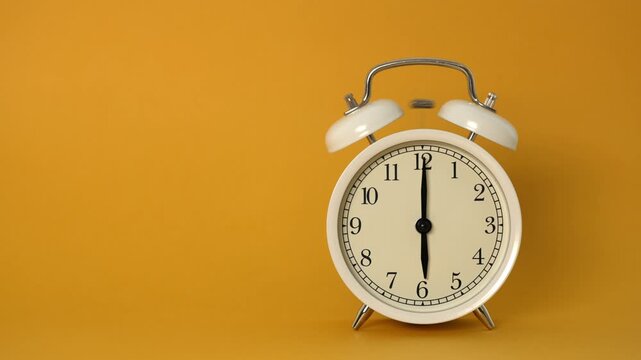 Classic white twin-bell alarm clock ringing loudly at six o'clock in the morning, vibrating and shaking on a vibrant yellow-orange background with ample copy space for text or graphics