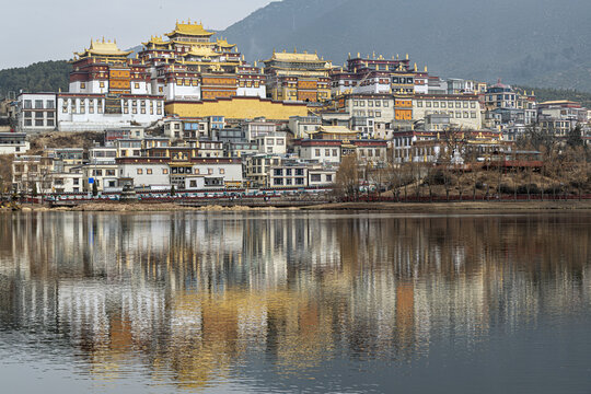 View of the golden-roofed Songzanlin Monastery cascading down the hillside, mirrored serenely in the lake's still waters, Shangri-La, Yunnan, China.