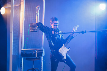 Fototapeta premium Crazy artist performing live show in studio, playing electric guitar and singing heavy metal music. Cool funky singer doing alternative rock performance with leather jacket and dark make up.