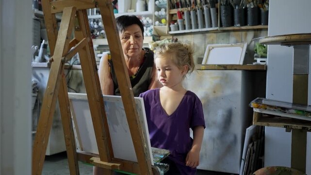 Child painting with an grandmother in a cozy art studio. Candid indoor moment of creativity and learning. Artistic lifestyle scene with real people and natural light.
