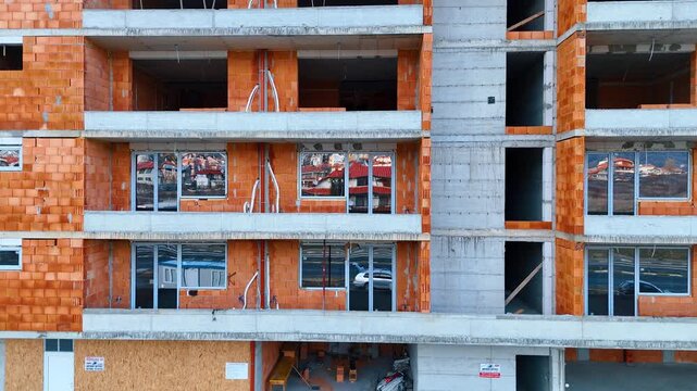 Close up of apartment building facade under construction with brick walls. Exterior view of a multi-story residential building showing red brickwork and concrete balconies without railings.