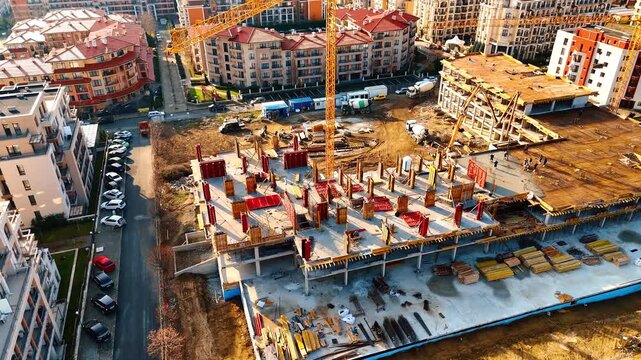 Workers and machinery on building frame at construction site. High angle shot of metal reinforcement and concrete formwork