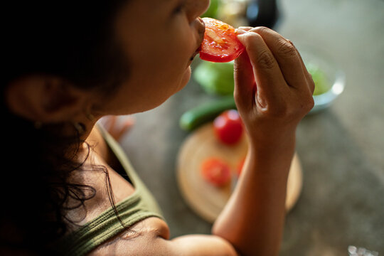 Woman eating fresh tomato slice in home kitchen, close-up