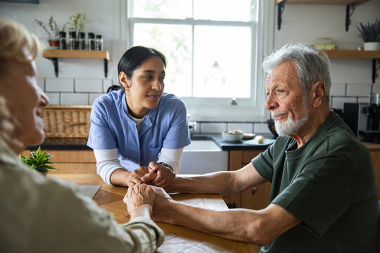 Home caregiver comforting senior man at kitchen table