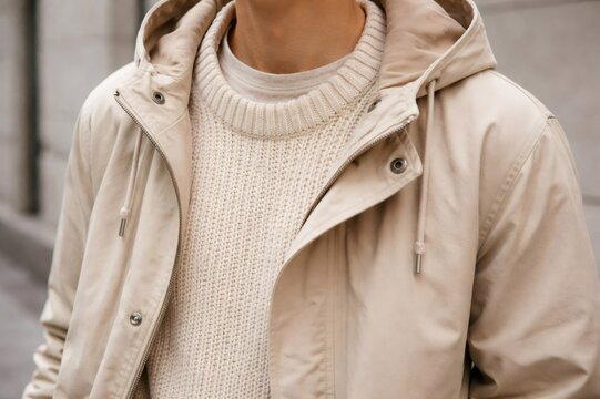Person wearing a warm, stylish combination of a cream colored chunky knit sweater and an outer hooded jacket in neutral beige tones, showcasing casual fashion and comfort