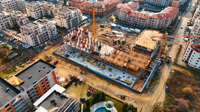 High angle view of construction site with tower cranes and machinery. Wide drone shot showing heavy machinery and tower cranes at a large scale building development project.