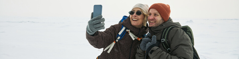 Header of Caucasian woman and man smiling and taking selfie with smartphone outdoors in snowy...