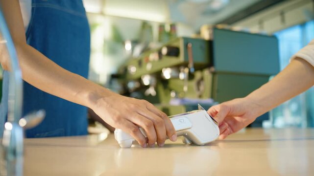 Customer paying with card at cafe counter terminal. Female hand holding payment device while receiving card. Cashless transaction happening during purchase. Close view of service process inside cafe.