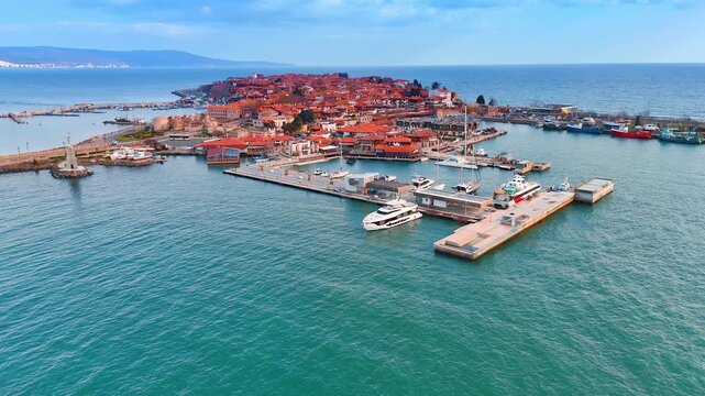 Aerial view of a modern yacht marina near an old town. High angle shot of luxury yachts and boats docked at a white pier in turquoise sea water by the coast.