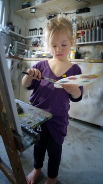 Preschool child focused on painting with brush and palette in a home art studio. Artistic expression, learning through creativity and play. Indoors, warm natural light.