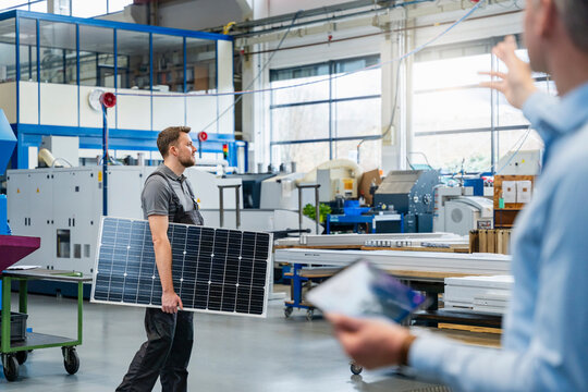 Employee carrying photovoltaic panel during meeting in production hall