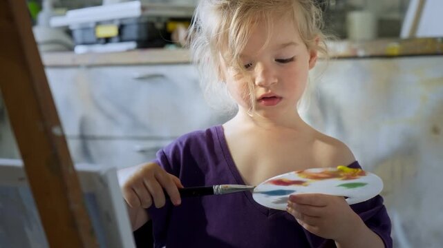 Preschool child focused on painting with brush and palette in a home art studio. Artistic expression, learning through creativity and play. Indoors, warm natural light.