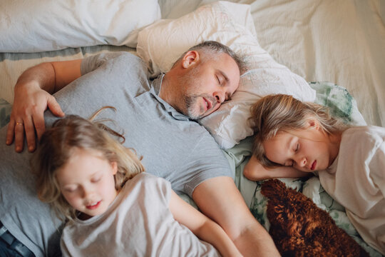 Father and daughters sleeping together in a cozy home environment