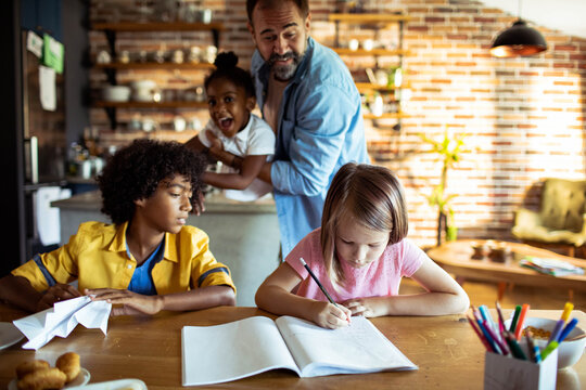 Father supervising kids doing homework at kitchen table at home