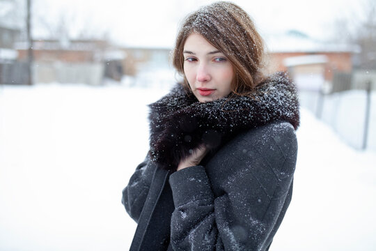 Woman in winter coat with fur collar standing outdoors in snow