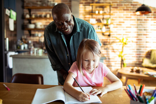 Adult man tutoring young girl at home kitchen table