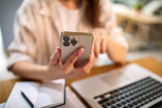Person using smartphone with laptop at home office desk