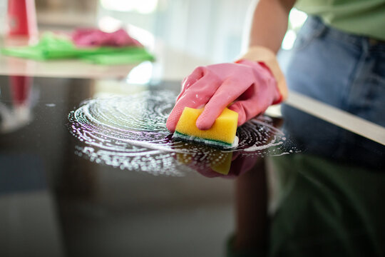 Person scrubbing kitchen glass stovetop with sponge