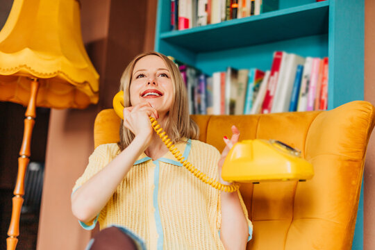 Smiling woman talking on retro yellow phone in stylish home interior