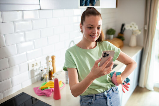 Young woman checking smartphone during kitchen cleaning