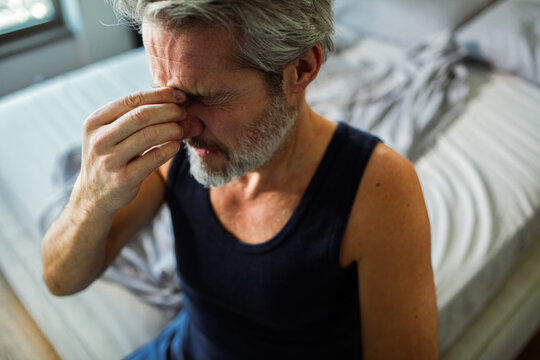 Middle-aged man with headache sitting on bed at home