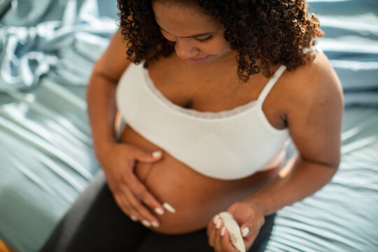 Expectant mother touching belly on bed at home