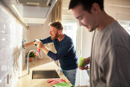 Two men cleaning tiled kitchen backsplash at home