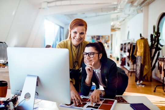 Two fashion designers collaborating at computer in modern studio