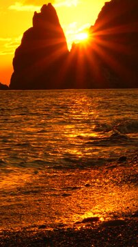 Sunset ocean mountains, golden sunlight shining through rugged peaks during a beautiful tranquil evening on the seashore.