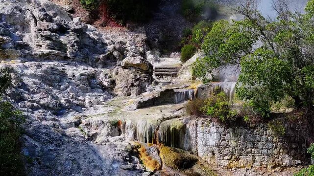 Aerial view of Furnas fumaroles where steam rises from geothermal vents, surrounded by dark rocks and contrasting volcanic textures in the Azores, Portugal.