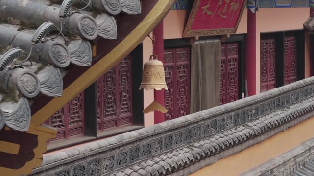 Static medium shot of an engraved golden bell hanging from a yellow painted beam, with ornate red lattice doors and grey carved roof tiles behind, at Luohan Temple in Chongqing, serene and sacred atmo