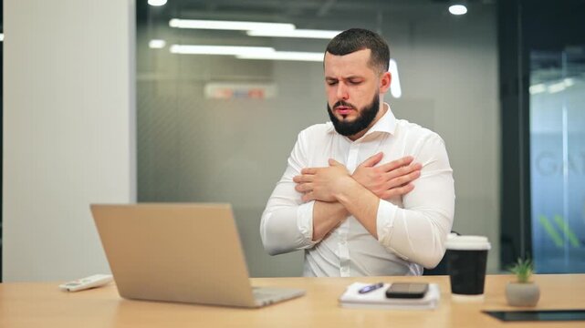 Young worker at office desk experiencing discomfort from cold temperature. Adjusts climate with remote control, seeking warmth. Feels relief from the chilly environment.