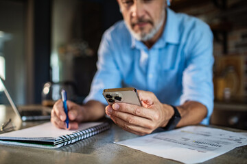 Mature man paying bills on smartphone at home