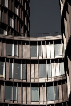 Curved modern office architecture with glass windows where urban reflections and linear patterns define a sleek facade in a contemporary city exterior composition