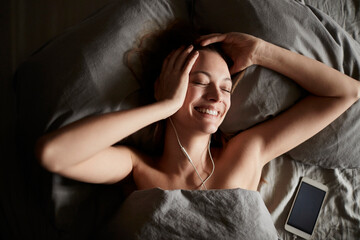 Fototapeta premium Smiling woman listening to music in bed at home