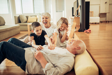 Grandparents tickling grandchildren on living room floor