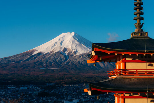 View of the snow-capped Mount Fuji rises majestically behind the vibrant red Chureito Pagoda, a symbol of serenity against the clear blue sky, Fujiyoshida, Chuerito Pagoda, Japan.