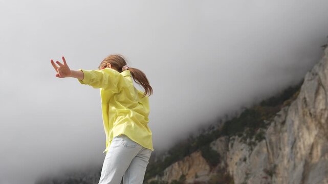 Girl mountain dancing, cheerful preteen spinning, enjoying freedom high above the dramatic clouds.